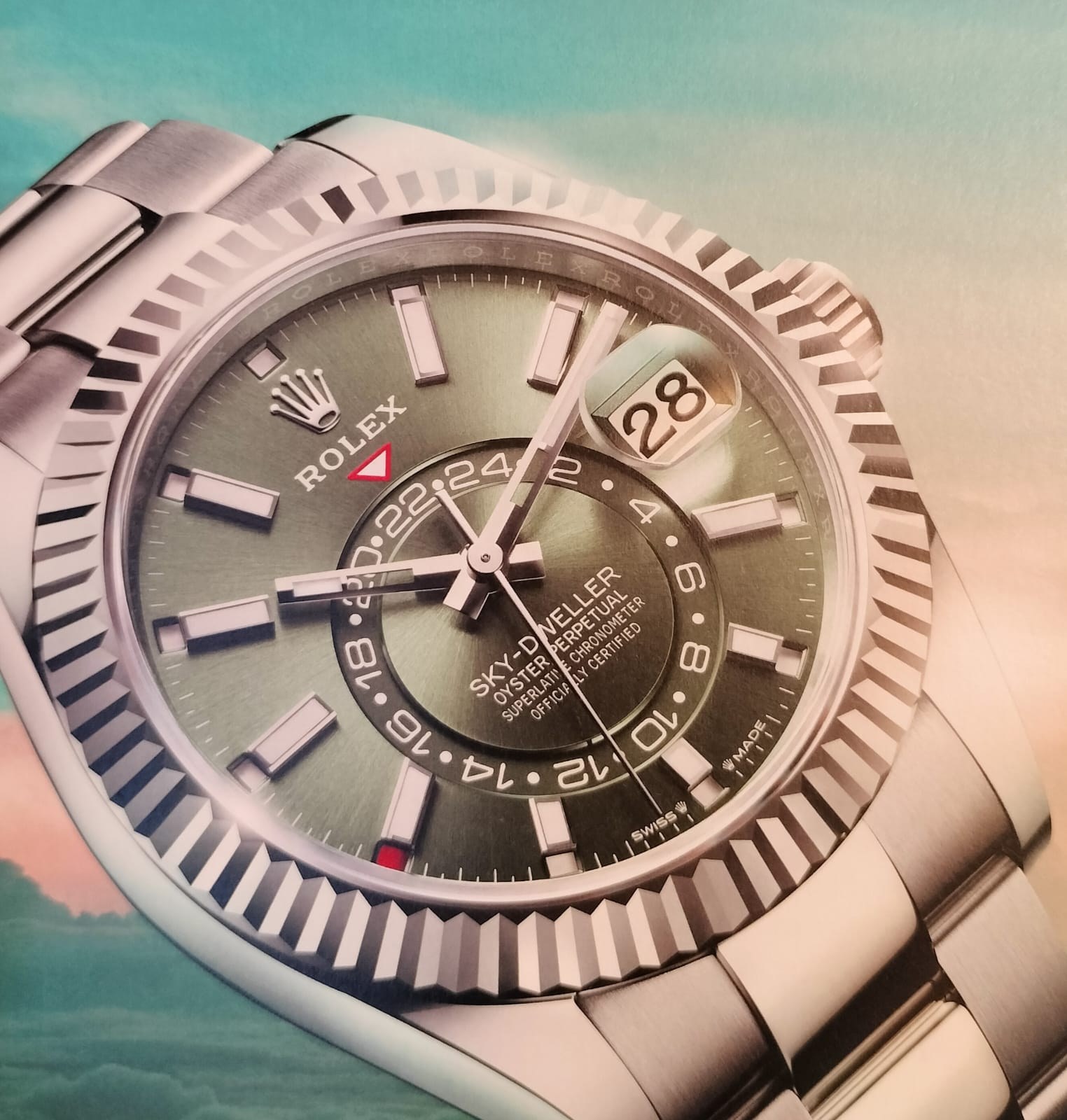 Close-up photograph of a Rolex Sky-Dweller with a white gold fluted Ring Command bezel, green sunray dial, off-center 24-hour disc and red month indicator at 8 o'clock
